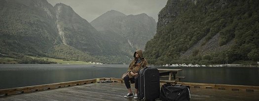 Hooded woman sitting on dock with suitcases