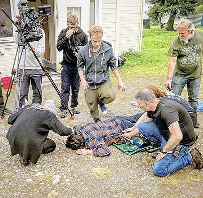 Behind the scenes shot - unconscious man on floor, surrounded by crew and camera