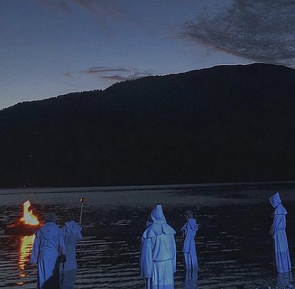 Hooded figures by water's edge, boat burning in water
