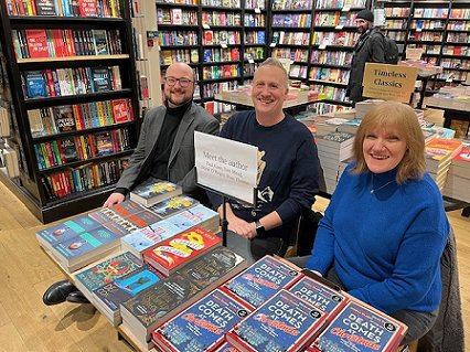 L to R: a smiling Tom Mead, Russ Thomas and Marie O'Regan, sitting behind a display of their books at Waterstones Orchard Square