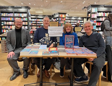 L to R: a smiling Tom Mead, Russ Thomas, Marie O'Regan and Paul Kane, sitting behind a table displaying their books