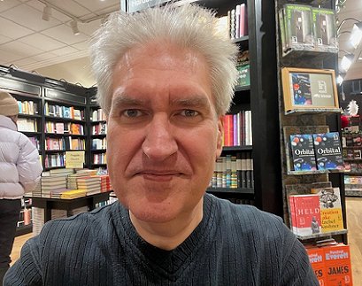 a smiling Paul Kane sitting in front of bookshelves at Waterstones Orchard Square