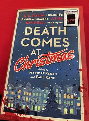 photograph of a copy of Death Comes at Christmas featuring a 'signed' sticker, on a red tablecloth