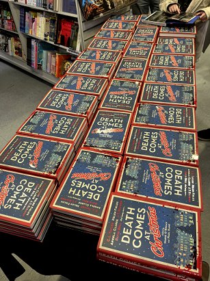 photograph of a display featuring many copies of Death Comes at Christmas, edited by Marie O'Regan and Paul Kane, piled up reaady for signing