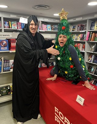 photograph of a scowling Russ Thomas, dressed as Death, pretending to strangle a shocked Tina Baker, dressed as a Christmas tree