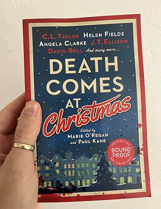 photograph showing a man's hand holding up a proof copy of Death Comes at Christmas, edited by Marie O'Regan and Paul Kane, against a white background