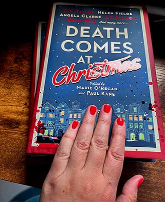 photograph of a woman's hand with red painted nails on top of two copies of Death Comes at Christmas, edited by Marie O'Regan and Paul Kane