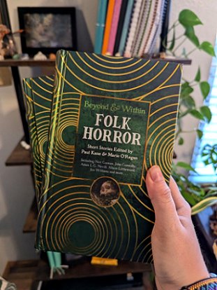 photograph of a woman's hand holding two contributor copies of Beyond and Within Folk Horror, edited by Paul Kane and Marie O'Regan