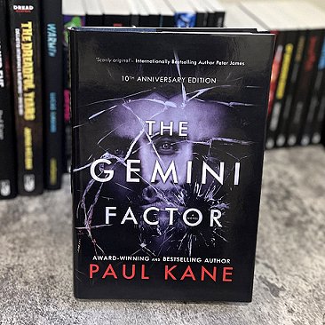 Book display. row of books standing on a marbled surface. In front, a copy of The Gemini Factor 10th Anniversary edition, by Paul Kane