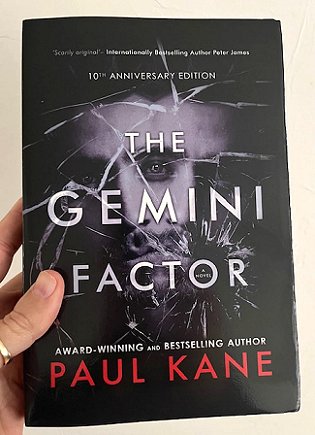 image of a man's hand holding up a copy of a book, The Gemini Factor, 10th Anniversary Edition, by Paul Kane