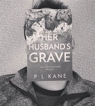 Person holding a copy of Her Husband's Grave by P L Kane in front of their face