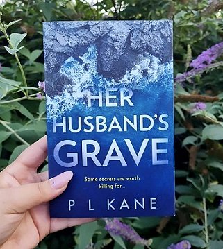 Woman's hand holding a copy of Her Husband's Grave by P L Kane