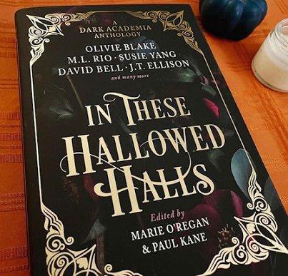 image showing a copy of In These Hallowed Halls, edited by Marie O'Regan and Paul Kane, lying on an orange cloth with a white candle in the background