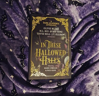 photograph showing a copy of In These Hallowed Halls, edited by Marie O'Regan and Paul Kane, lying on a fleece purple cloth decorated wtih bats and stars
