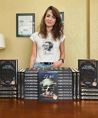 Photograph of author M L Rio standing behind a display of her novel If We Were Villains and the anthology In These Hallowed Halls, edited by Marie O'Regan and Paul Kane
