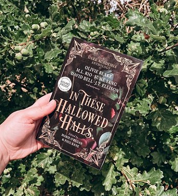 Picture of a hand holding a copy of In These Hallowed Halls, edited by Marie O'Regan and Paul Kane, against a background of an evergreen bush