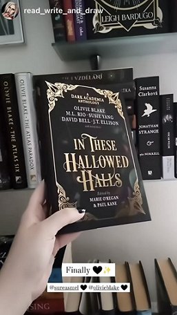 photograph of a woman's hand with black nail polish, holding up a copy of In These Hallowed Halls, edited by Marie O'Regan and Paul Kane. In the background are other dark academia books