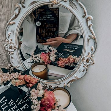 Picture showing a woman holding a copy of In These Hallowed Halls, edited by Marie O'Regan and Paul Kane, up so that it reflects in a mirror