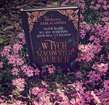 photograph of a copy of the Polish edition of In These Hallowed Halls, edited by Marie O'Regan and Paul Kane, standing up surrounded by pink flowers