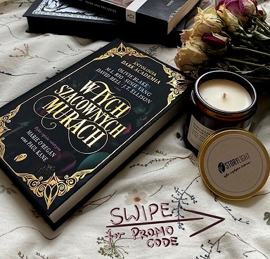 Copy of the Polish edition of In These Hallowed Halls, edited by Marie O'Regan and Paul Kane, lying on a cream cloth, beside a jar candle, dried flowers and two books.