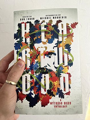 photograph of a man's hand holding a copy of Heartwood - A Mythago Wood anthology, edited by Dan Coxon, against a white background