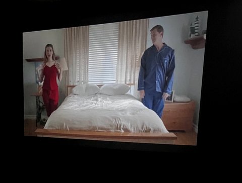 still image from Life-O-Matic short film. A woman and a man standing either side of a double bed