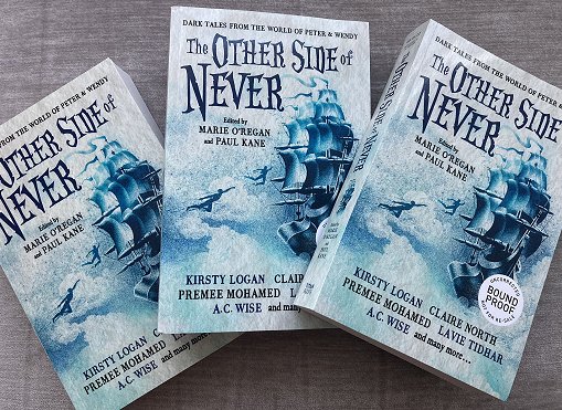 Image of three copies of the anthology The Other Side of Never, edited by Marie O'Regan and Paul Kane. Book cover features a ship sailing in the clouds, with the shadow of two figures flying towards it
