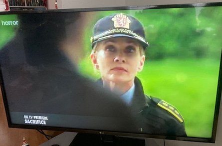 TV screen showing Barbara Crampton in police uniform. Still from Sacrifice movie
