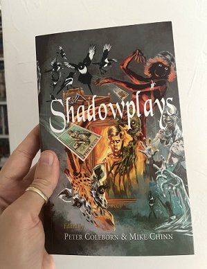 photograph of a man's hand holding up a copy of Shadowplays, edited by Peter Coleborn and Mike Chinn