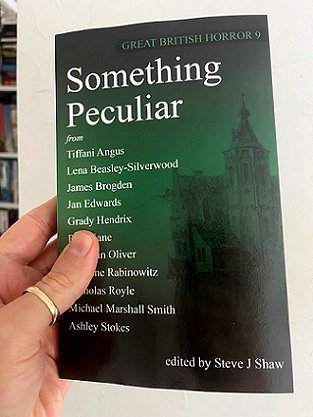 photograph of a man's hand holding up a copy of Something Peculiar. Great British Horror 9, edited by Steve J Shaw.