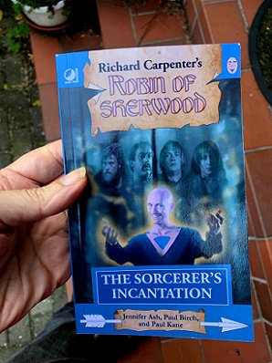 photograph showing a hand holding a copy of The Sorceror's Incantation, by Jennifer Ash, Paul Birch, and Paul Kane