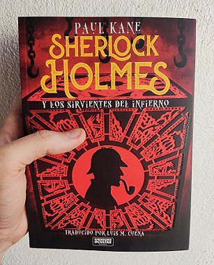 A man's hand holding a copy of the Spanish edition of Sherlock Holmes and the Servants of Hell by Paul Kane, against a cream wall