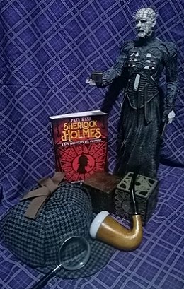 display showing a copy of the Spanish edition of Sherlock Holmes and the Servants of Hell, by Paul Kane. ALongside a magnifying glass, a deerstalker hat, a meerschaum pipe, a puzzlebox, and a figure of Pinhead, against a blue check background