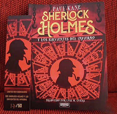 photograph showing a copy of the Spanish edition of Sherlock Holmes and the Servants of Hell by Paul Kane, plus a bookmark for the book, on a red and black background