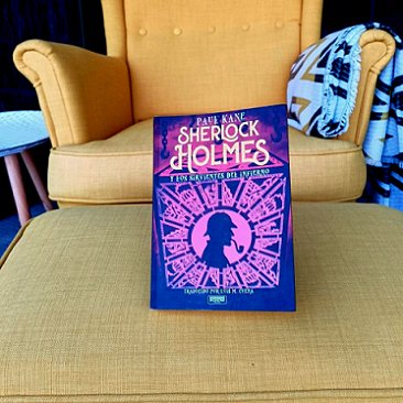 photograph of a copy of the Spanish edition of Sherlock Holmes and the Servants of Hell on a footstool, in front of a mustard-coloured armchair