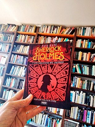 photograph of a hand holding a copy of the Spanish edition of Sherlock Holmes and the Servants of Hell by Paul Kane up against a bookcase