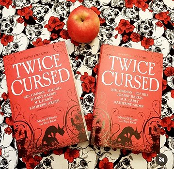 Book display featuring an apple and two copies of Twice Cursed, edited by Marie O'Regan and Paul Kane on a cloth with black and white skulls and red roses