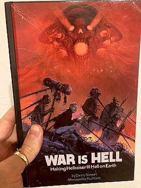 Man's hand holding a book: War is Hell: Making Hellraiser III Hell on Earth by Danny Stewart, afterword by Paul Kane