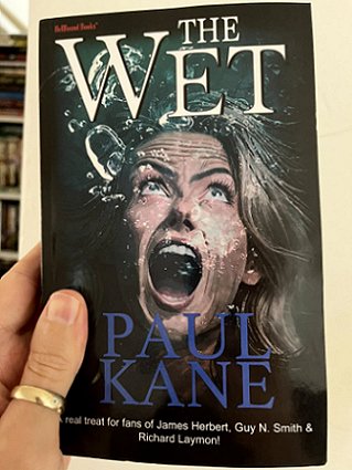 photograph of a man's hand holding up a copy of the book The Wet by Paul Kane. Text reads A reat treat for fans of James Herbert, Guy N. Smith and Richard Laymon