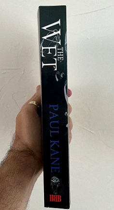 photograph of a man's hand holding up a copy of The Wet by Paul Kane to show the spine of the book