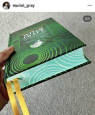 screenshot from @muriel_Gray, of a hand holding up a copy of Beyond and Within Witchcraft, edited by Marie O'Regan and Paul Kane, to show the spiral page edges and gold ribbon. In the background is a grey surface.