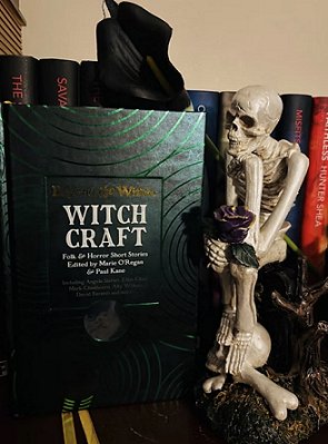 photograph showing a copy of Beyond and Within Witchcraft, edited by Marie O'Regan and Paul Kane, standing alongside a sitting model of a skeleton, in front of a row of books
