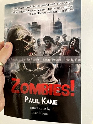 A man's hand holding a copy of the book Zombies! by Paul Kane