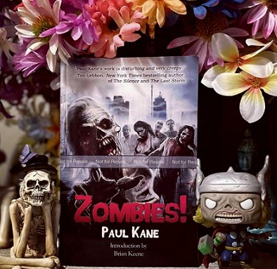 Display featuring standing copy of Zombies! by Paul Kane, surounded by a zombie Thor figure and a figure with a skull face, in front of flowers