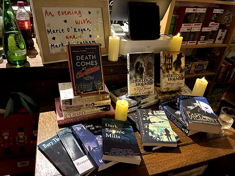 candlelit book display featuring Death Comes at Christmas, edited by Marie O'Regan and Paul Kane, and various titles by Marie and by Mark A. Latham. Sign at the back reads An evening with Marie O'Regan and Mark A. Latham