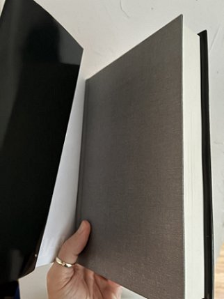 photogrpah of a man's hand holding up a copy of Short Sharp Shocks by Paul Kane, to show the black board cover under the dustjacket