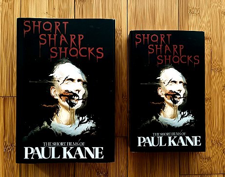 photograph showing a hardback and a paperback copy of Short Sharp Shocks by Paul Kane, on a wooden surface
