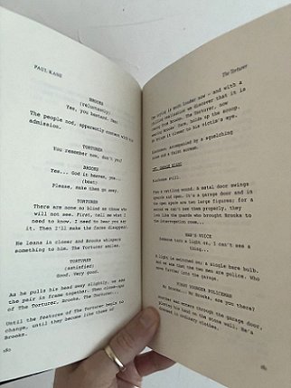 photograph showing a man's hand holding a copy of Short Sharp Shocks by Paul Kane, open to show two script pages