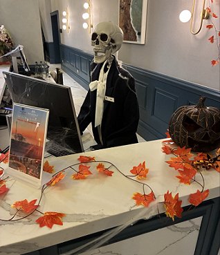 photograph showing a reception desk decorated with pumpkins and autumn leaves for Halloween, featuring a skeletal receptionist