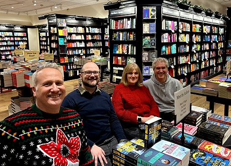 L to R: Russ Thomas, Tom Mead, Marie O'Regan and Paul Kane, sitting at a table displaying their books, including Death Comes at Christmas, edited by Marie O'Regan and Paul Kane